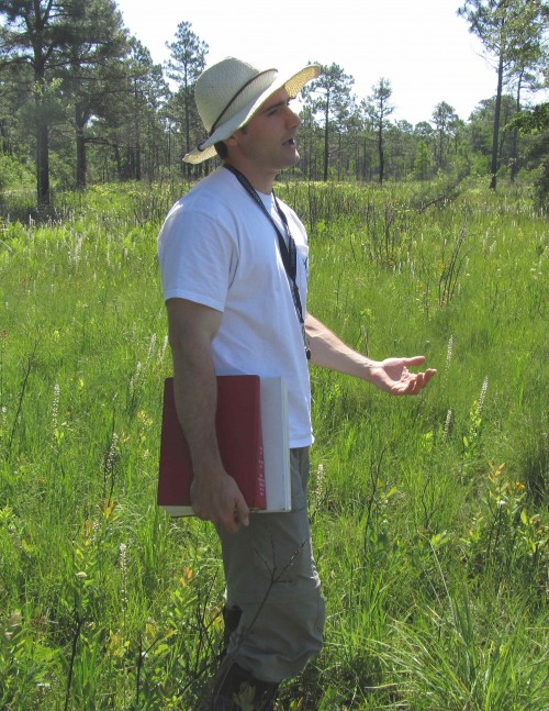 Robert Thornhill stands in a green field talking to a group that is not shown